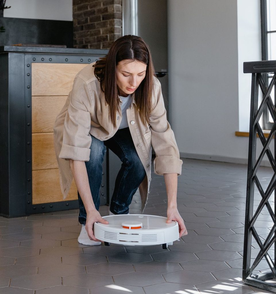 Image of a woman lifting a robot vacuum off the floor.